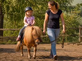 Kind reitet auf Shetty-Pony beim Bambini-Ponyreiten in Renningen, Mutter führt das Pony.