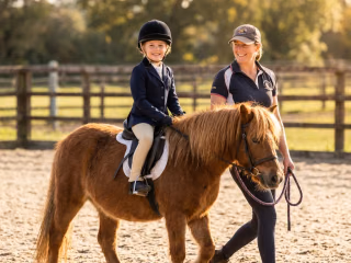 Kind auf einem Pony mit Trainerin