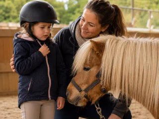 Vorsichtiges Kind berührt ein kleines Pony, während eine Erwachsene ruhig danebensteht