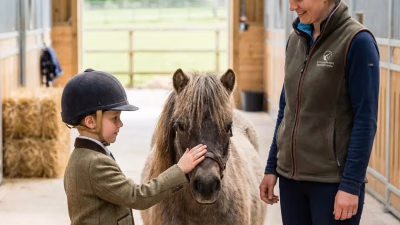 Kind steht ruhig neben einem kleinen Pony und hält den Führstrick locker in der Hand