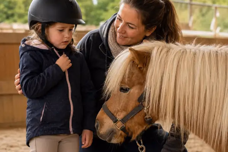 Vorsichtiges Kind berührt ein kleines Pony, während eine Erwachsene ruhig danebensteht