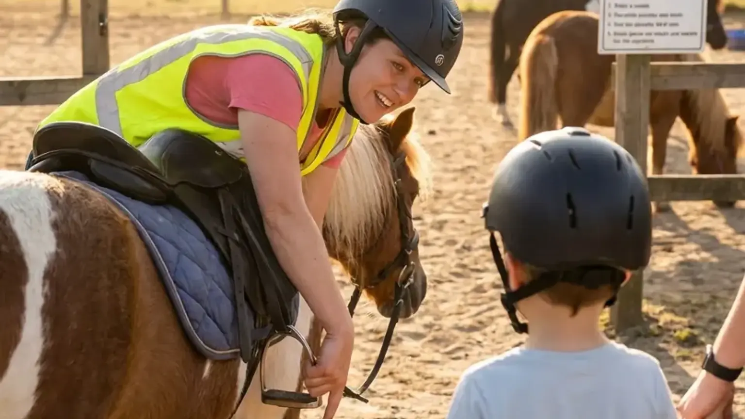 Kind mit Reithelm streichelt ruhig ein Pony auf dem Hof