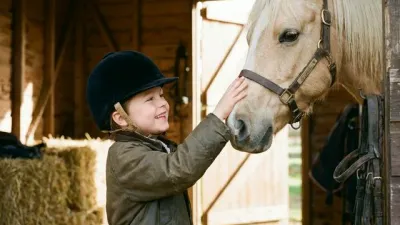 Kind mit Reithelm streichelt ein Pony auf dem Ponyhof